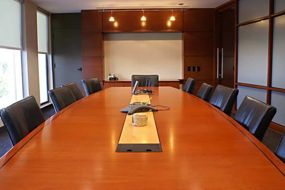 Large brown wood conference table surrounded by black leather chairs.
